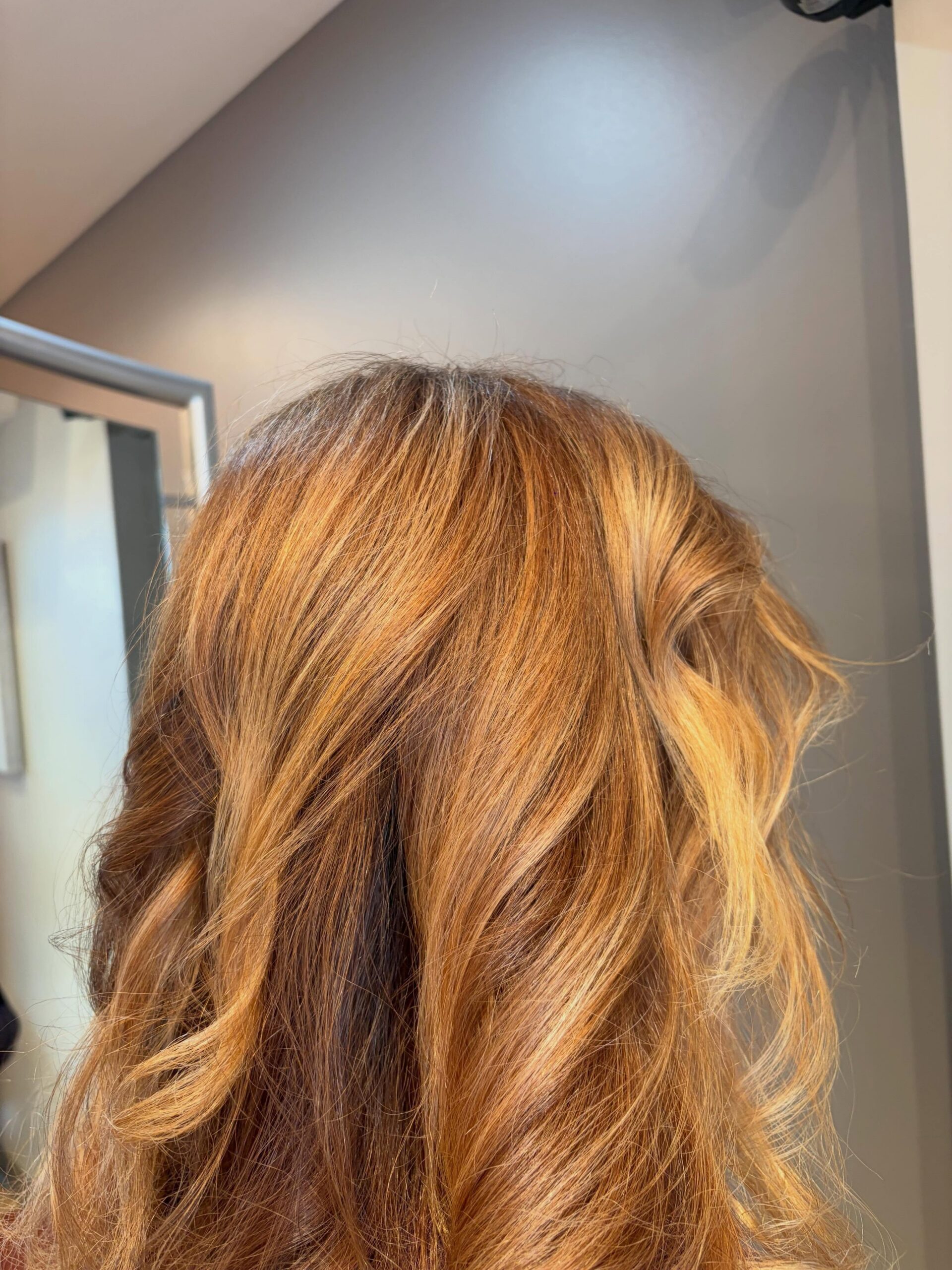 Close-up of warm brown hair with subtle golden highlights, photographed from above in a mirror-lit room.