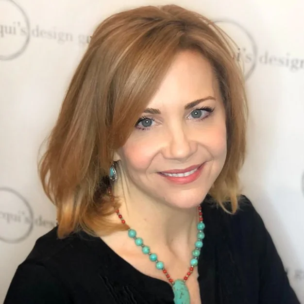 Smiling woman with shoulder-length strawberry blonde hair wearing turquoise beaded necklace and turquoise earrings against a light backdrop.