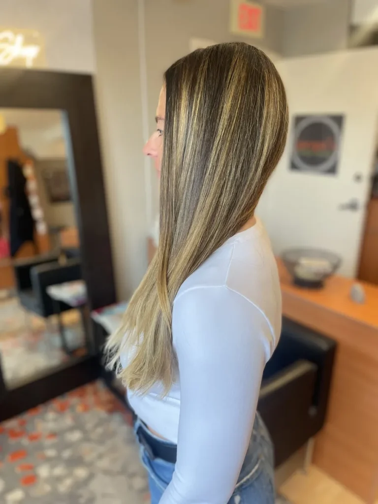 Side view of a woman with long straight hair and blonde highlights in a salon setting.