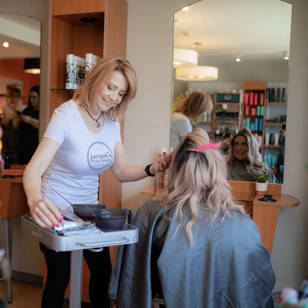 A colorist preparing color for a blonde client at Jacqui's Design Group in Arlington, MA