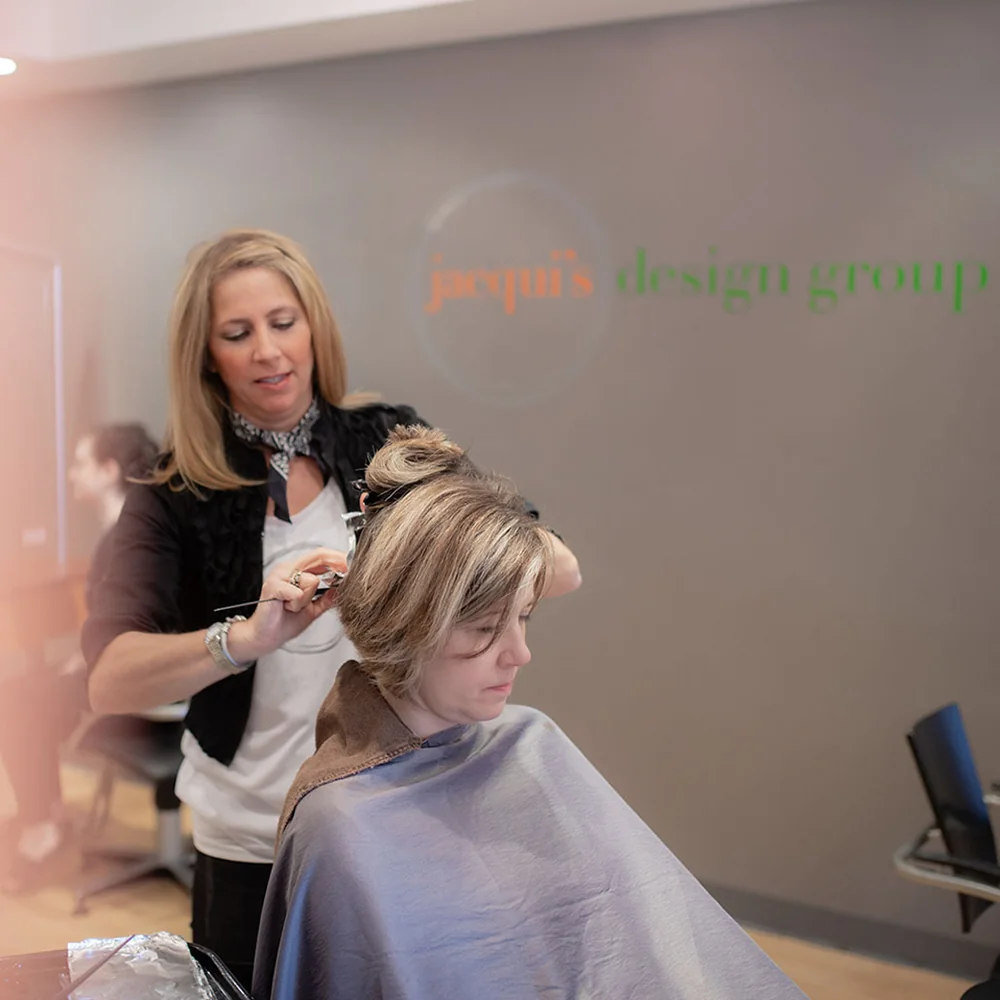 Hairdresser trims a woman's hair in a salon, client wearing a cape.