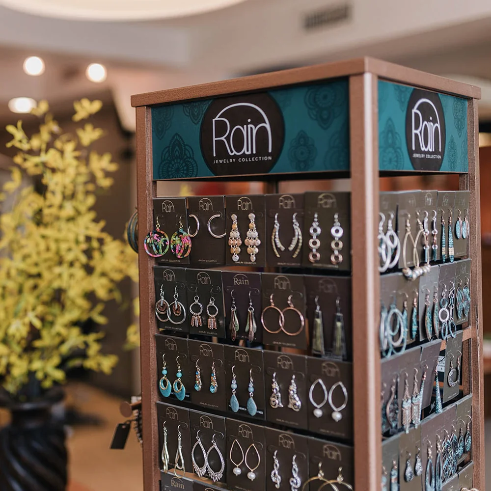 Earring display rack with multiple pairs from Rain Jewelry Collection on teal branding panels and black display cards nearby.