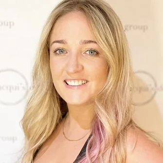 Head-and-shoulders portrait of a smiling blonde woman with wavy hair, against a light backdrop.