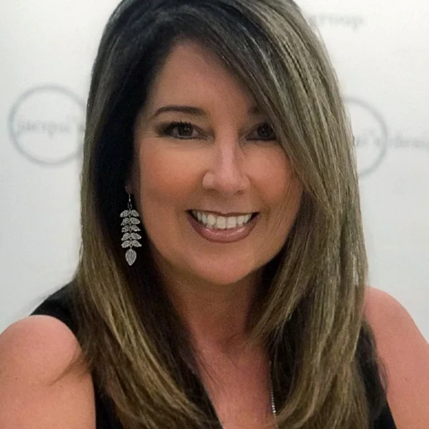 Smiling woman with shoulder-length hair and silver leaf earrings, posing for a photo.